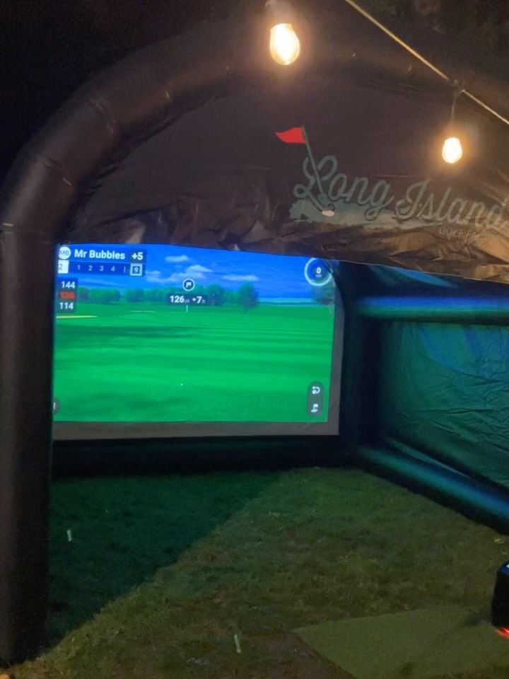 Long Island Golf Factory simulator lit up at night under string lights, with a golf hole on the screen